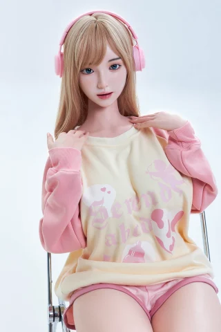Doll in pastel pink and yellow oversized sweatshirt, wearing pink headphones, with long straight blonde hair, seated pose.