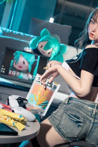 Subject features a doll with long hair in a casual pose, wearing a black crop top and denim shorts. The setting includes gaming consoles, snacks, and vibrant blue lighting.
