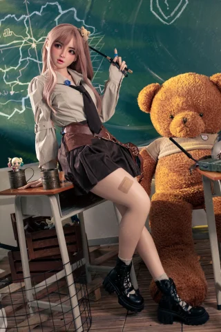 Subject features a doll with long, light pink hair, wearing a white shirt and dark skirt. She poses confidently beside a large teddy bear in a classroom setting, with a chalkboard in the background. The outfit includes a tie and knee-high socks,