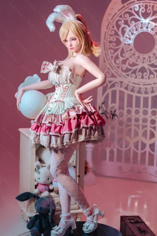 Pose features a playful stance with one hand on her hip. She wears a frilly dress in pink and cream, complemented by white fishnet stockings and bunny ears. The setting includes a whimsical backdrop with soft pastel colors and plush toys.