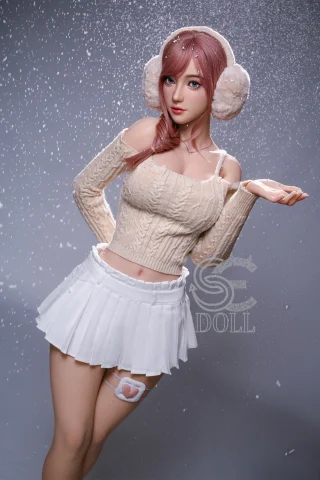 A doll with long pink hair and fluffy earmuffs wears a cream-colored off-shoulder sweater and a white pleated skirt, posing with one hand raised as if catching snowflakes against a soft, snowy background.
