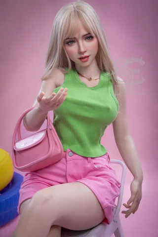 A doll with long blonde hair wears a green ribbed tank top and pink shorts, seated with a pink handbag against a pastel pink background.