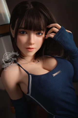 A realistic doll with long brown hair, wearing a blue sleeveless top, poses with one hand in her hair, showcasing a soft expression.