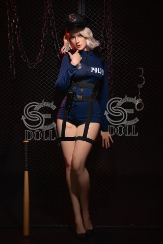 A doll dressed in a blue police uniform with a fitted design, wearing a cap and high heels, poses confidently against a dark, chain-link background.