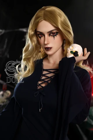 A doll with long, wavy blonde hair, wearing a dark, laced top, holds a skull in one hand, featuring dramatic makeup with black tears.