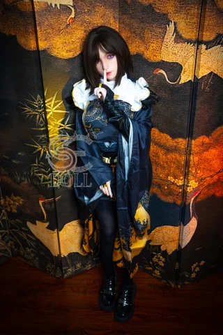 A doll with short dark hair, wearing a black and gold outfit, stands against a patterned backdrop featuring cranes and bamboo.