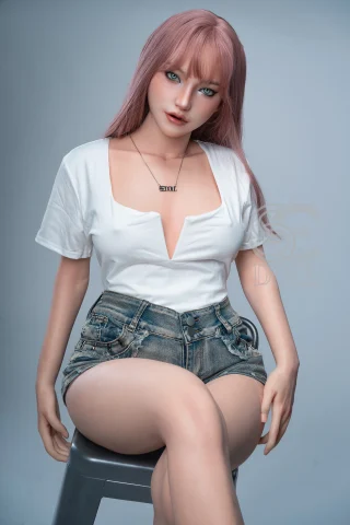A realistic doll with long pink hair, wearing a white deep V-neck shirt and denim shorts, seated on a stool against a neutral background.