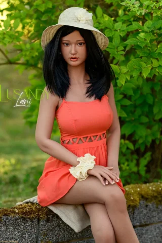 Lani 161cm Lusandy silicone doll in a stylish orange dress and hat, set against a lush green background.