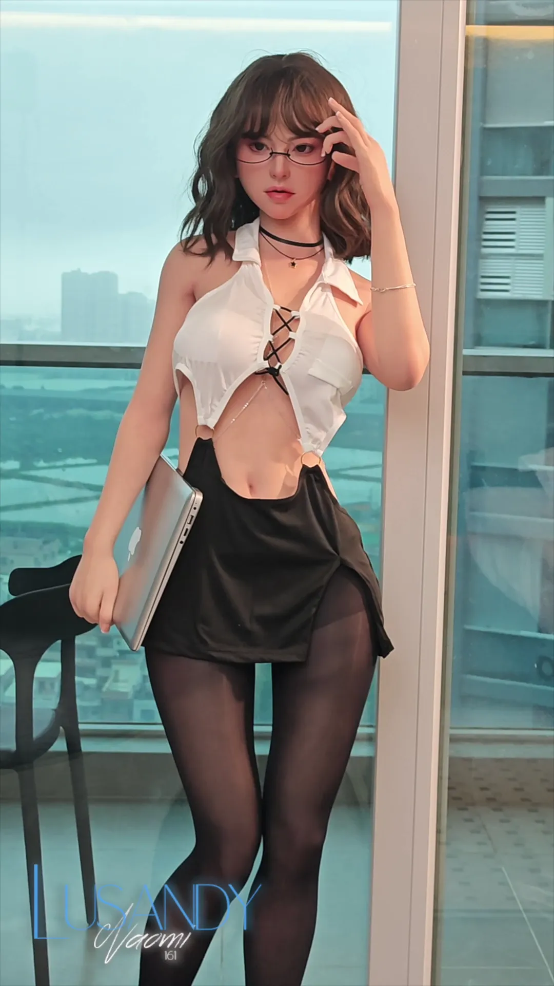 lusandy promo pic Naomi 161cm stands in a modern setting wearing a white cropped shirt and black mini skirt, holding a laptop.