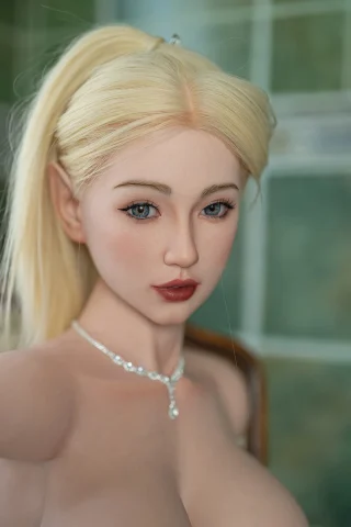 Aurora 85cm G-Cup doll with blonde hair, blue eyes, and wearing a silver necklace, posed in a softly lit setting.