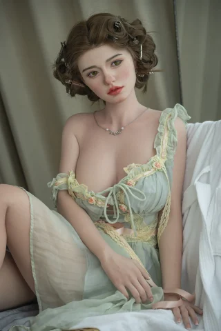 Natalia doll, 171cm, C-cup, wearing a light green dress with floral accents, posed sitting with soft curls and natural makeup.