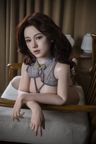 Nina 151cm C-Cup doll in a sheer gray top, posed on a wooden chair with a soft background.